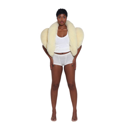 woman wearing a pale yellow shearling vest over a white tank top and shorts standing on a white background